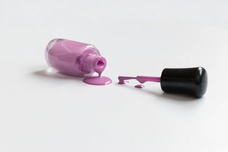 Dripping pink nail polish bottle next to applicator brush with white backgroundの写真素材
