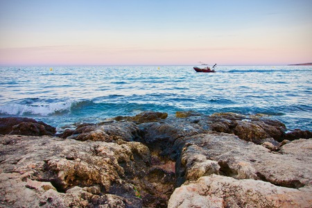Small boat on blue ocean at a cliff at sunset, conceptual of summer vacationsの写真素材