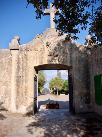 Historic entrance to a church courtyard surmounted by a cross above an open doorway with a view through to a tarred road in the backgroundの写真素材