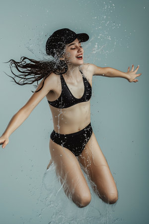 Young beautiful woman in black swimsuit and cap splashing water, studio shotの素材