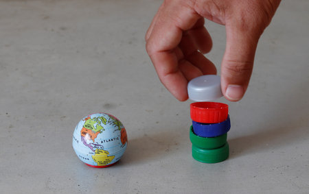 Small earth globe next to hand stacking pet bottle caps representing plastic pollution and the need...