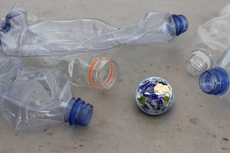 Pet plastic bottles pointing at planet earth globe on grey surface. Showing plastic pollution,...