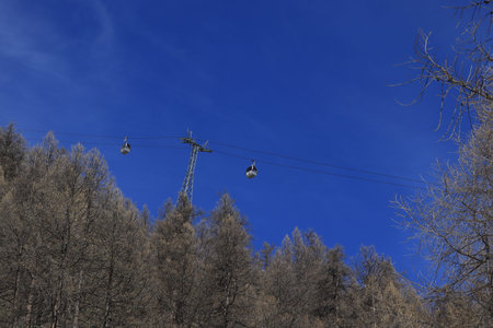 Gondola passing in front of alpine snow mountains and blue sky.