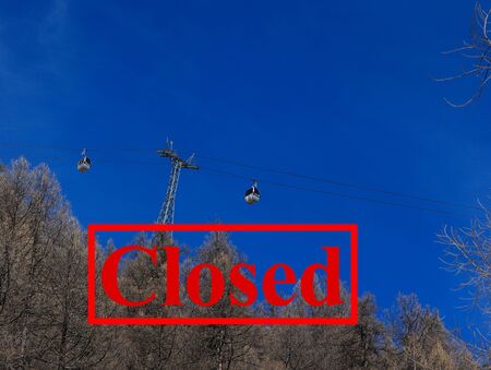 Closed ski slopes and resorts due to Coronavirus outbreak. Measures to stop spreading of pandemic. Gondola above winter forest against blue ski.の写真素材
