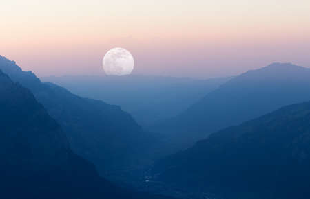 Sunset with layered mountain landscape and moon at end of valley.の写真素材