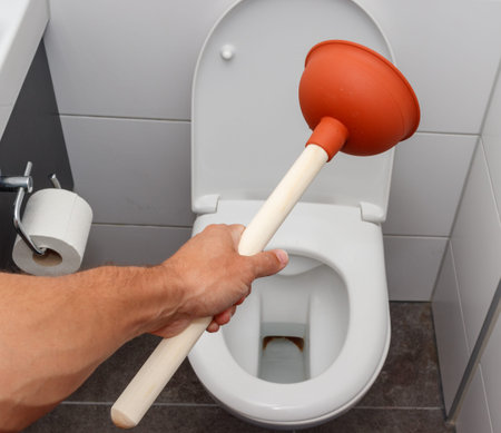 Young man using plunger to unclog a toilet bowl.の写真素材