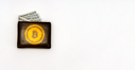 Bitcoin on black leather wallet with hundred dollar bills sticking out. New virtual money cryptocurrency concept.の写真素材