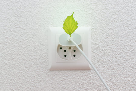 Phone charger in electric socket or wire plug with green leaf symbolizing green energy and...