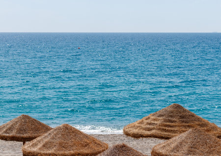 summer vacation near sea concept poster style picture with straw umbrella on horizon line between water surface and empty sky on background with space for copy or text.の写真素材