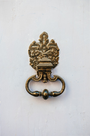 Ancient vintage copper door knocker as seen on a white painted wooden surfaceの写真素材