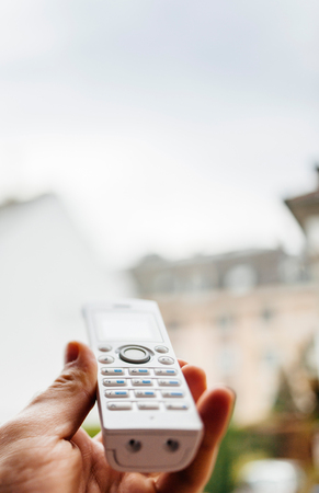 Hand holding cordless phone to the window for better signal. Shallow depth of field with the focus on the phoneの写真素材