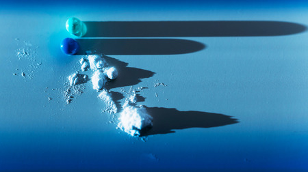 Capsule pill content ingredient scattered on blue medical background with lateral light and long shadowsの写真素材