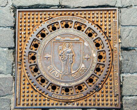 TRIER, GERMANY - 22 FEV 2015: Detail shot of Trier - Treves manhole cover on cobblestone pavement featuring the iconic city logo - MOnk with Bible and Kay. Trier or Treves is the oldest city in Germany. It is also the oldest seat of a bishop north of the のeditorial素材