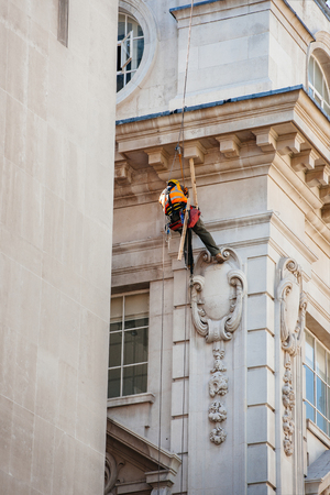 Construction worker lowers himself into position to perform maintenance high up of a building in London while using safety equipment and providing job securityの写真素材