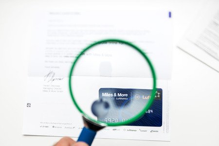 PARIS, FRANCE - JANUARY 14, 2015: Man looking through a magnifying glass to the new Miles  More Classic card from Lufthansa Airlinesのeditorial素材