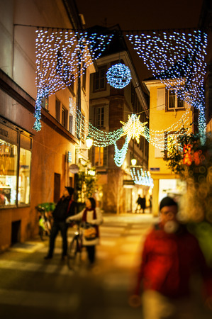 Defocused view of couple admiring window shoppting of a store at the traditional Christmas market in the historic Strasbourg, Alsace, France with illuminated lights above the streetの写真素材
