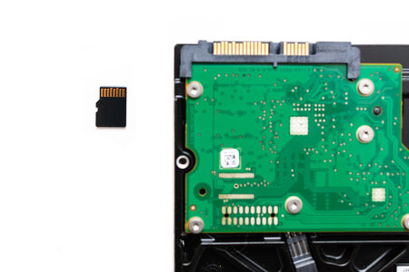 Focus on Micro SD Secure Digital card next to HDD Hard Disk Drive on white background - comparing...