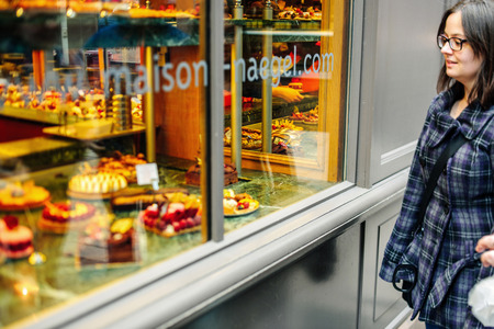 STRASBOURG, FRANCE - MARCH 21, 2015: Woman admiring French sweet pastry food in typical French boulangerie saloon - tilt-shift defocused viewのeditorial素材