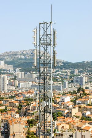 Telecommunication tower with multiple antennas and data transmitters with beautiful city in the background and wide mountain areaの写真素材
