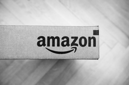 PARIS, FRANCE - JAN 28, 2016: Amazon logotype printed on cardboard box side, seen from above on a wooden floor. Amazon Inc is the an American electronic e-commerce companyのeditorial素材