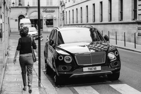 PARIS, FRANCE - MAY 21, 2016: Woman admiring the luxury Bentley Bentayga Hybrid SUV on the streets...