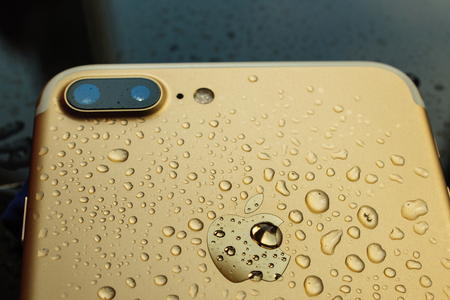 PARIS, FRANCE - SEP 26, 2016: New Apple iPhone 7 Plus unboxing and testing - pure gold iphone covered with rain water. New iPhone7 is one of the best waterproof smart phone in the worldのeditorial素材