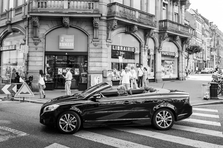 Black and white view of senior man driving beautiful Volvo C70 Convertible car crossing pedestrian walk in the center of the French city of Strasbourg, Alsace on a summer day with pedestrians and touristsのeditorial素材