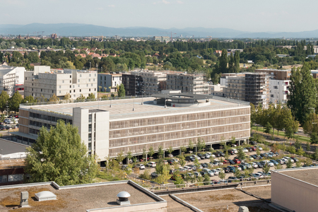 Aerial view of a modern garage building parking lot with multiple, cars parked on a summer day - buildings, factories and mountains in the backgroundのeditorial素材