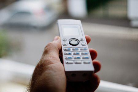 Cordless phone in hand against window. Tilt-shift lens used to accent the center of the phone and to emphasize the attention its central buttonsの写真素材
