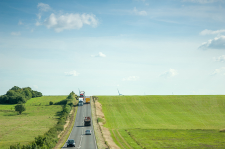 Aerial view of highway with two lane wih cars, trucks adn motorcycles driving between green fields and wind mills behind the hillsの写真素材