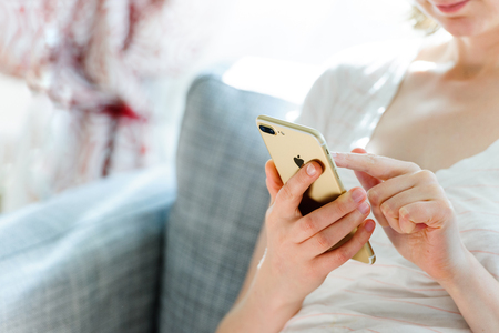 PARIS, FRANCE - SEP 29, 2016:  New Apple iPhone 7 plus display in woman's hands - she is testing the camera and overall presentation sitting on the couch in home environment.  New Apple iPhone tends to become one of the most popular smart phones in the woのeditorial素材