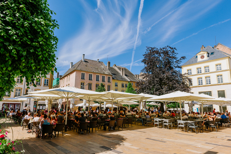 THIONVILLE ,FRANCE - JUNE 10, 2016: Full cafe beer restaurant terrace in center of old french city of Thionville, France with couples, friends and families drinking, eating surrounded by green trees and beautiful blue skyのeditorial素材