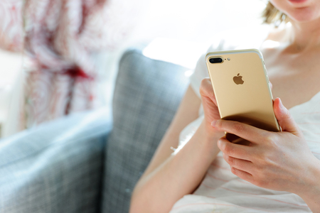 PARIS, FRANCE - SEP 29, 2016: Woman testing the New Apple iPhone 7 plus display, camera and overall presentation sitting on the couch in home environment.  New Apple iPhone tends to become one of the most popular smart phones in the world in 2016のeditorial素材