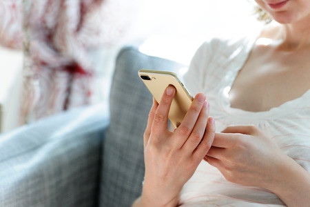 Woman testing the smartphone, camera and overall presentation sitting on the couch in home environmentの写真素材