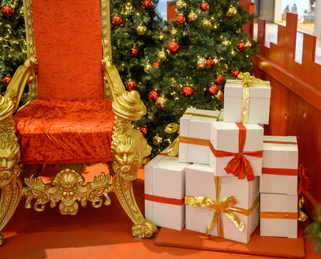 Christmas gifts presents boxes near luxurious red chair Santa Claus throne surrounded by multiple gift boxesの写真素材