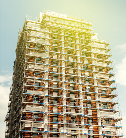 Construction scaffolding on a tall skyscraper building against blue sky, low angleの写真素材