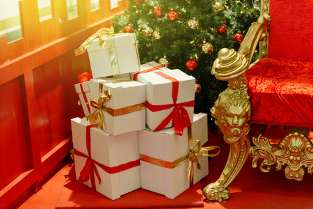 Elegant Christmas gifts presents boxes wraped with red ribbon near luxurious red chair Santa Claus throne surrounded by multiple gift boxesの写真素材