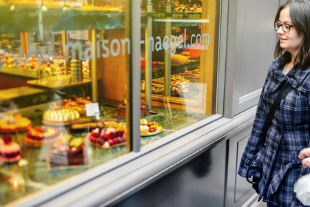 STRASBOURG, FRANCE - MARCH 21, 2015: Woman admiring French sweet pastry food in typical French boulangerie saloon, admiring delicious food - tilt-shift defocused viewのeditorial素材