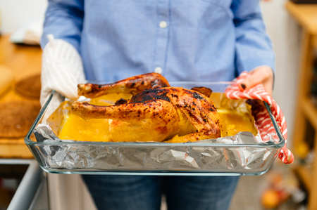 Woman holding a roast chicken directly from oven made under special Swedish recipe with ginger, oranges, apples and other organic food ingredients - ready to be servedの写真素材