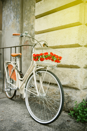 White vintage bicycle with red flowers parked against a wall in Pisa, Italy on a bright sunny dayの写真素材
