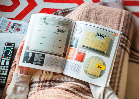 PARIS, FRANCE - AUGUST 24, 2014: View from above of woman reading IKEA Catalogue before buying commode storage furniture for her new house. The catalogue is published annually by the Swedish home furnishing retailerのeditorial素材