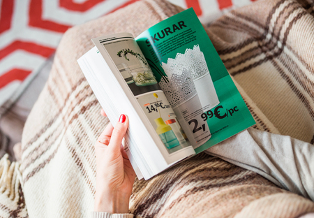 PARIS, FRANCE - AUGUST 24, 2014: Busy woman reading IKEA Catalogue before buying furniture for her new house. The catalogue is published annually by the Swedish home furnishing retailerのeditorial素材