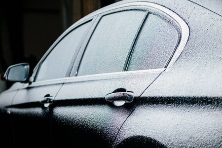 Right side of a luxury car covered with snow at night in the parkingの写真素材