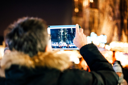 Rear view of tourist taking photo on tablet of the impressive Notre-Dame cathedral in Strasbourg at night during winter holidaysのeditorial素材