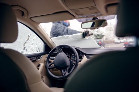 View from inside the car of woman cleaning the car windshield from snow after a snow stormの写真素材