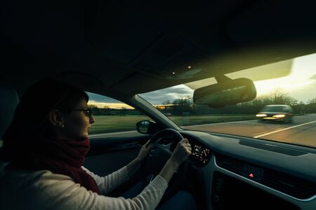 Woman driving on German autobahn at dusk taking care of the coming from the fron car security highwayの写真素材