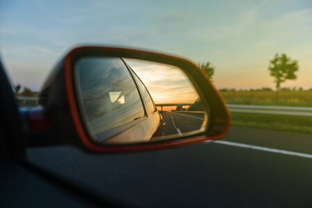 Vintage look of road and trees reflected in rear-view mirror while driving through agricultural fieldの写真素材