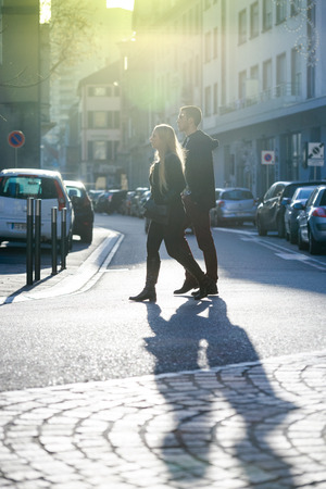 MULHOUSE, FRANCE - DEC 19, 2015: Youg male and yopung female French couple walking on a French street with beautiful sunflare behind them in Mulhouse, Franceのeditorial素材