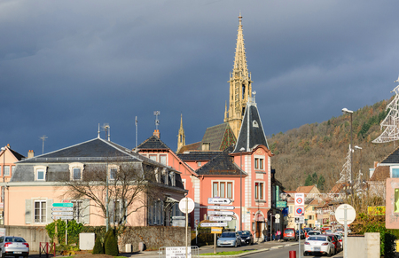 THANN, FRANCE - DEC 12, 2015: Majestic spire of Collegiale Saint-Thiebaut (Saint-Theobald collegiate church) in Thann, Haut-Rhin peacefully watching the city of Thann on a warm winter day with dark cloud approaching in the backgroundのeditorial素材