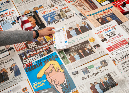 PARIS, FRANCE - JAN 21, 2017: Man holding lottery ticket abovemajor international newspaper journalism featuring headlines with Donald Trump inauguration as the 45th President of the United States in Washington, D.Cのeditorial素材